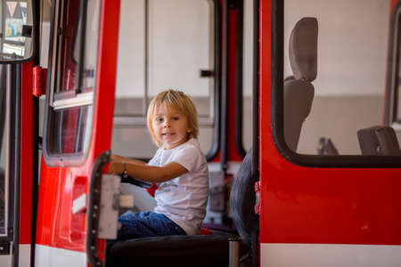 Child, cute boy, dressed in fire fighers cloths in a fire station with fire truck, childs dreamの写真素材