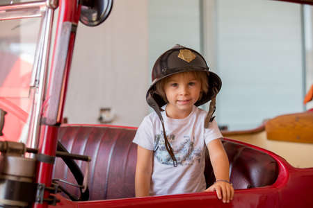 Child, cute boy, dressed in fire fighers cloths in a fire station with fire truck, childs dreamの写真素材