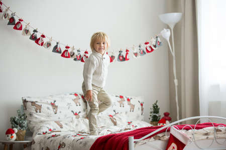 Beautiful toddler child, reading book in bed on Christmas, decoration around himの写真素材