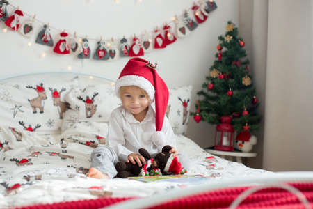 Beautiful toddler child, reading book in bed on Christmas, decoration around himの写真素材