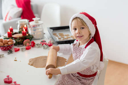 Cute blond child, boy and his mom, baking christmas cookies at home, having funの写真素材