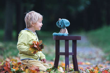 Little toddler child, boy, playing with knitted amigurumi dog toy in autumn park, autumntimeの写真素材