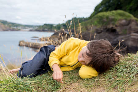 Children, enjoying quiet cloudy day on the ocean shore on the cliff, rocky beach in Englandの写真素材