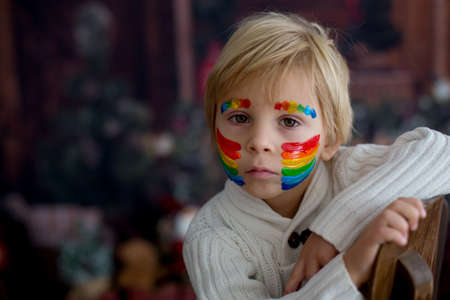 Beautiful child, toddler boy with painted face with rainbow, posing for close portrait in studioの写真素材