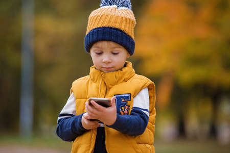 Happy child, playing with phone in the park, calling mommy, autumn pictures taken in the park,...