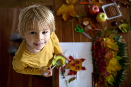 Sweet child, boy, eating avocado while applying leaves using glue while doing arts and chraft with leaves, colorful spectrum of leavesの写真素材