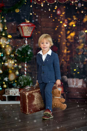 Cute child, holding suitcase and teddy bear, waiting at home for holidays, studio shotの写真素材