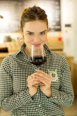 Young attractive woman, tasting wine in a wine store, enjoying glass of tasty red or white wineの写真素材