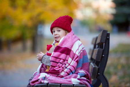 Happy child, playing with in autumn park on a sunny day, foliage and leaves all around him, eating...