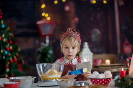 Cute blond child, toddler boy, baking christmas cookies at home, having funの写真素材