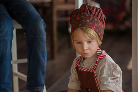 Angry toddler child, sitting under the table, while siblings preparing christmas cookies, sad child on christmasの写真素材