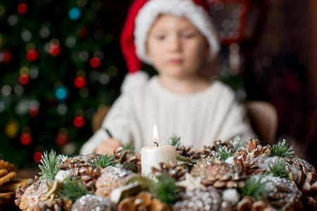 Advent wreath with burning candle in the middle, child writing letter in the background, christmas tree behindの写真素材