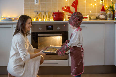 Cute blond child and his mother, baking christmas cookies at home, having funの写真素材