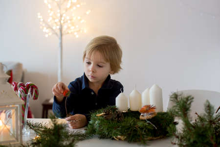 Cute toddler blond child, boy, decorating christmas advent wreath at homeの写真素材