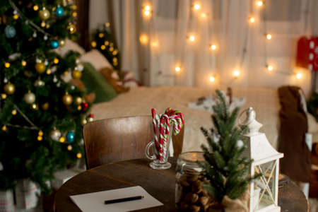 Old wooden table with christmas decoration and chair, paper prepared for writing, candy canes and nuts on the table and decoration in ther roomの写真素材