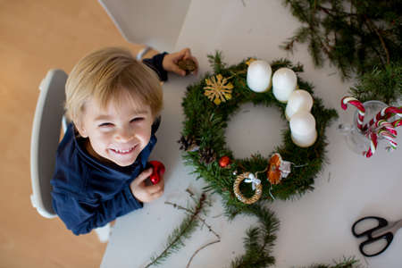 Cute toddler blond child, boy, decorating christmas advent wreath at homeの写真素材