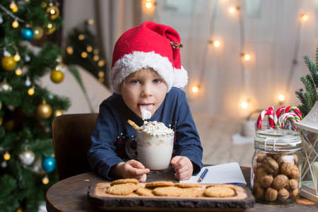Beautiful blond toddler child, boy, drinking hot cocoa with wipped cream, christmas decoration...