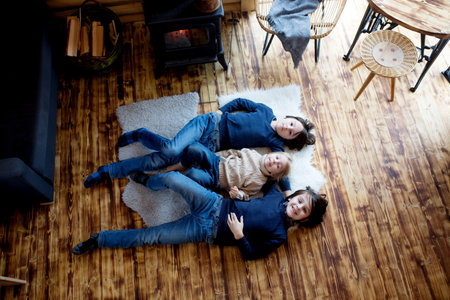 Three sweet children, siblings lying on the floor in little fancy wooden cottage, reading a book, drinking teaand enjoying cozy atmosphereの写真素材
