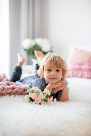 Cute toddler blond child with shirt, sitting on the bed with Valentine decoration, isolated backgroundの写真素材