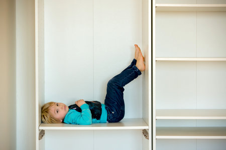 Cute child, sit in a white box in open wardrope, making funny facesの写真素材