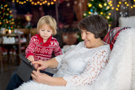 Cute child and grandmother, sitting on a cozy armchair at home on Christmas, playing together,...
