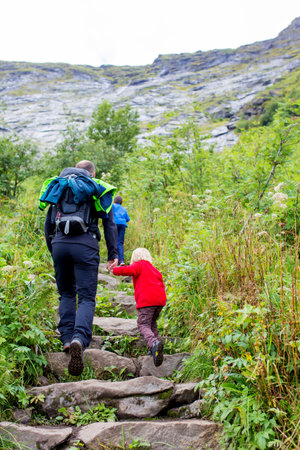 Children, toddler, brothers and father, climbing the stairs to Reinebringen, trekking path leading to the top of the mountain, where one can see Reine village and many fjords from aboveの写真素材