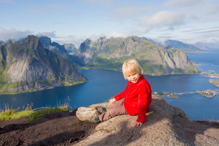 Cute child, standing on top of the mountains and looking down on Reine after climbing Reinebringen treeking path with lots of stairs, Lofoten, northern Norwayの写真素材
