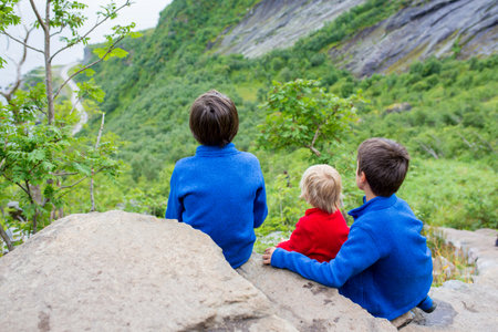 Children, toddler, brothers and father, climbing the stairs to Reinebringen, trekking path leading to the top of the mountain, where one can see Reine village and many fjords from aboveの写真素材