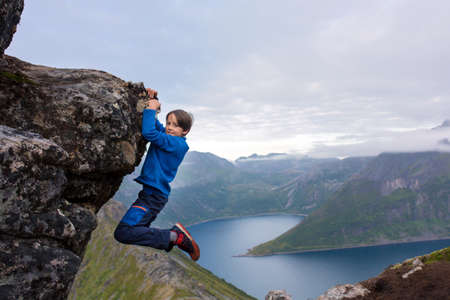 Happy child, hanging from a rock over Segla mountain on Senja island, North Norway. Amazing...