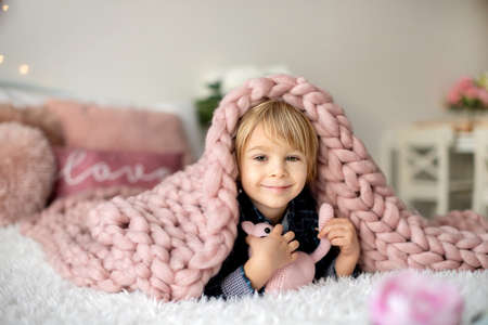 Cute toddler blond child with shirt, sitting on the bed with Valentine decoration, isolated backgroundの写真素材