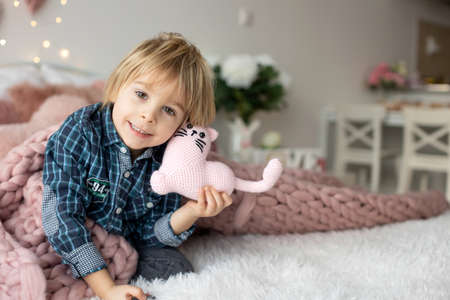 Cute toddler blond child with shirt, sitting on the bed with Valentine decoration, isolated backgroundの写真素材