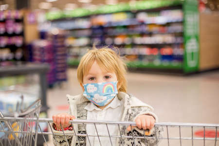 Cute toddler child, boy, wearing medical mask in supermarket store during covid pandemic lockdownの写真素材