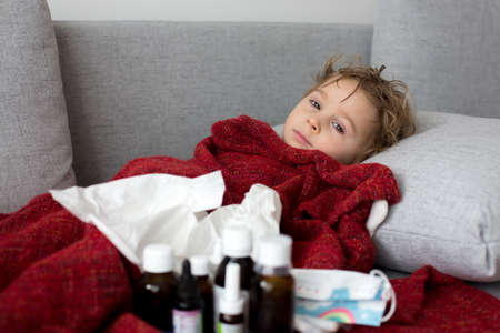 Toddler child, boy, lying sick on the sofa, mother checking himの写真素材