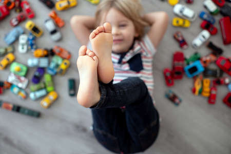 Cute toddler child, blond boy, playing with colofrul cars, different sizes and colors on the floor,...
