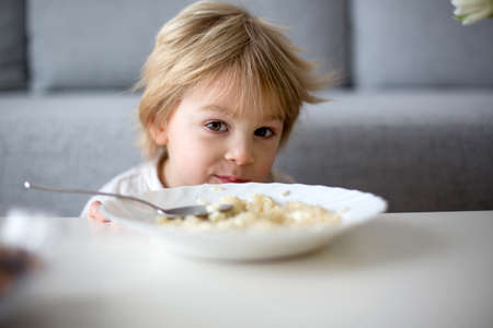 Cute toddler boy, eating pasta with white cheese at home for lunchの写真素材