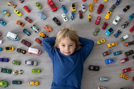 Cute toddler child, blond boy, playing with colofrul cars, different sizes and colors on the floor, smilingの写真素材