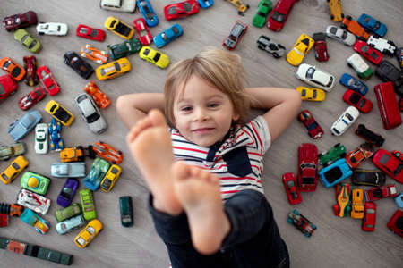 Cute toddler child, blond boy, playing with colofrul cars, different sizes and colors on the floor,...