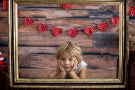 Cute toddler blond child, cute boy with valentine decoration, love, flowers, sitting on armchair...