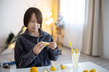 Cute preteen child, long hair boy, licking lemons at home and drinking lemonade, making funny facesの写真素材
