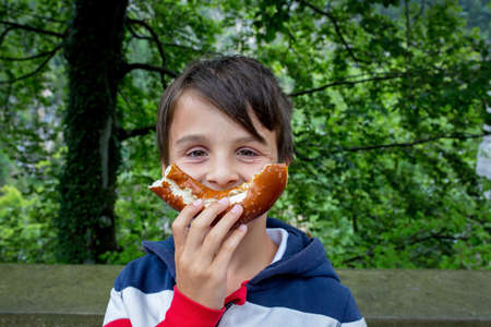 Cute little preschool child, holding big pretzel, smiling happily and eating
