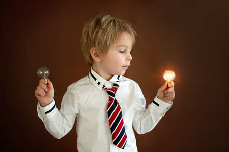 Cute toddler child, boy with smart casual clothing on isolated background, holding light bulbs, studio shotの写真素材