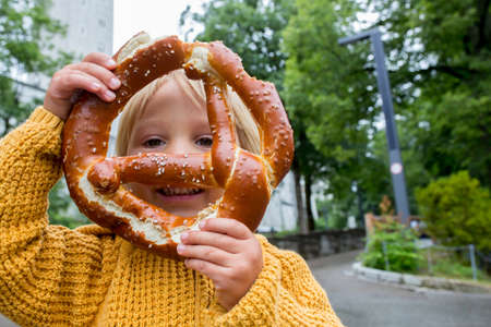 Cute little preschool child, holding big pretzel, smiling happily and eatingの写真素材