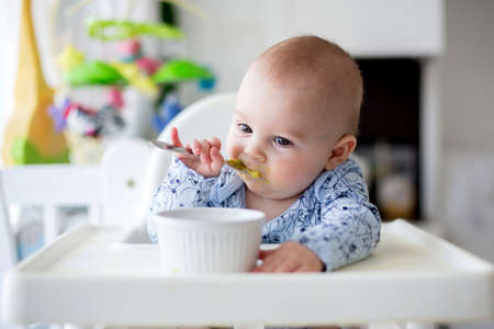Cute little baby boy, eating mashed vegetables for lunch, mom feeding him, sweet toddler boy, smilingの写真素材