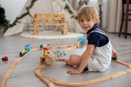 Cute blond toddler child, boy, playing with colorful trains and railroad at home on the floorの写真素材