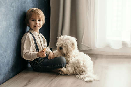 Cute blond preschool boy, sitting on the floor with pet dog, punished for mischief, angry at mom