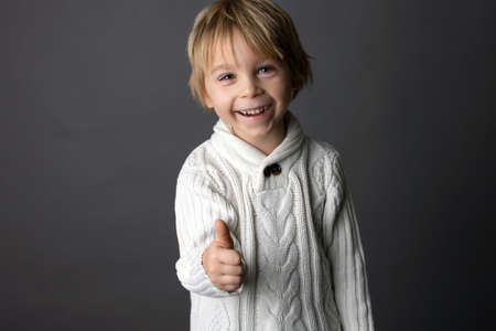 Cute little toddler boy, showing  YES gesture in sign language on gray background, isolated image, child showing hand singsの写真素材
