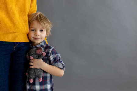 Sad little child, blond boy, hugging his mother at home, holding teddy bear