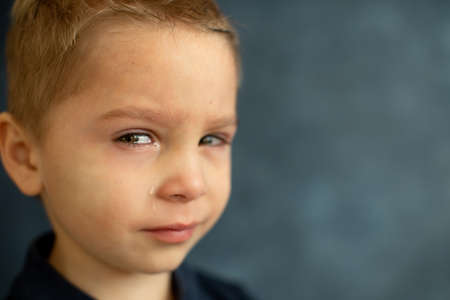 Sad little child, blond toddler boz, crzing, image isolated on blue background