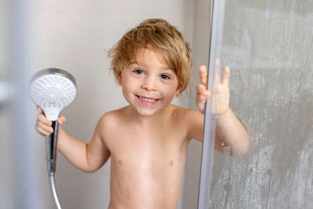 Sweet toddler boy in bathroom, taking shower, smiling happily at the cameraの写真素材