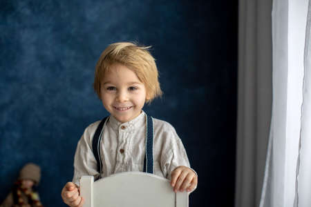 Cute portrait of blond preschool child, boy, on blue background, holding toyの写真素材